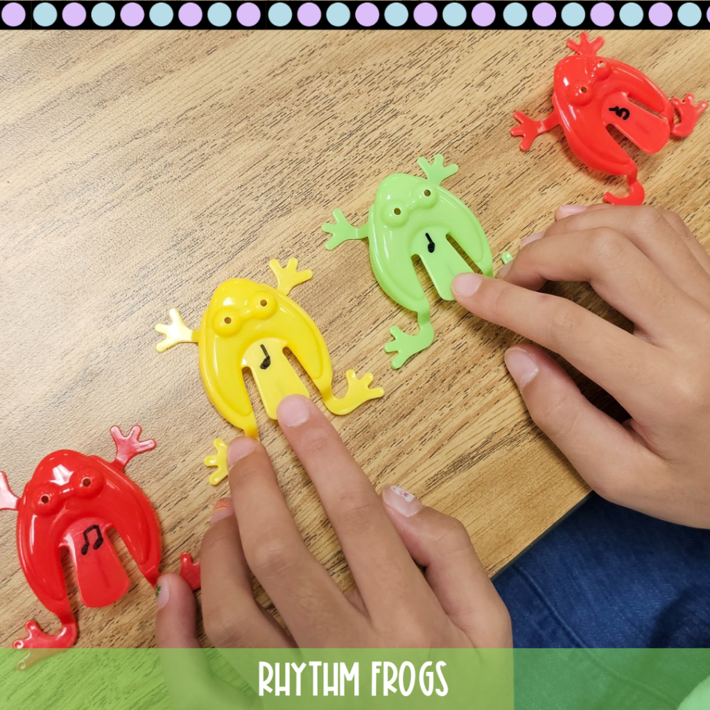 Four plastic frogs with different rhythms, an eighth note, quarter notes, and a quarter rest are on a desk. A child's hands are getting ready to launch the rhythm frogs