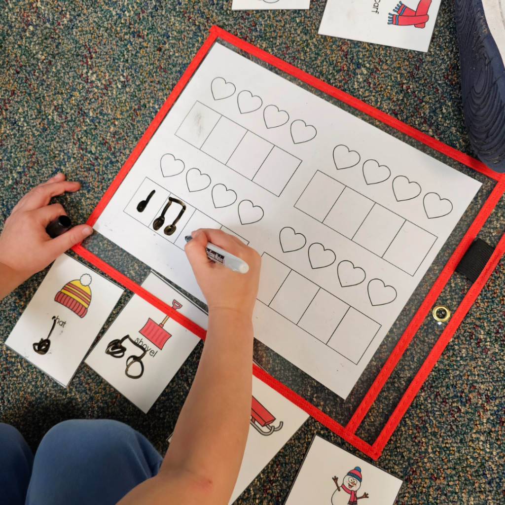 A student is using a dry erase marker to complete a rhythm activity tucked inside a red dry erase pouch. 